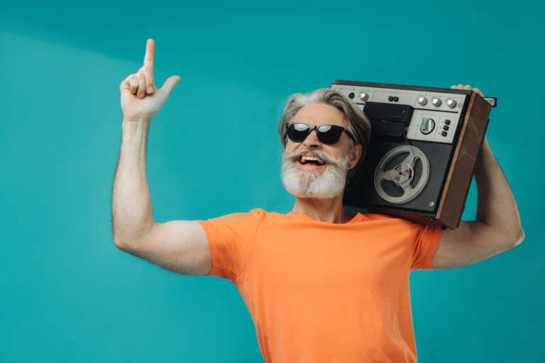 Gray-haired senior man cheerfully posing with record player on yellow background